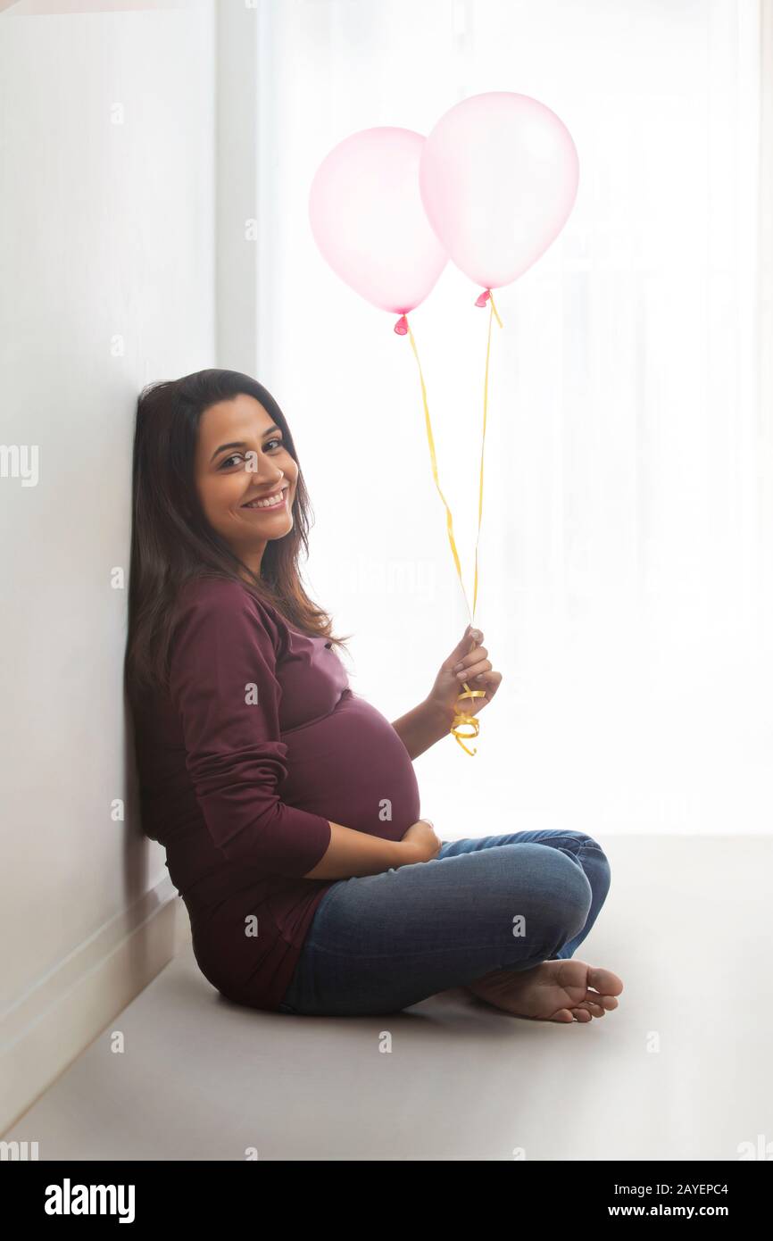Pregnant woman sitting with balloons in her hand and smiling Stock Photo -  Alamy