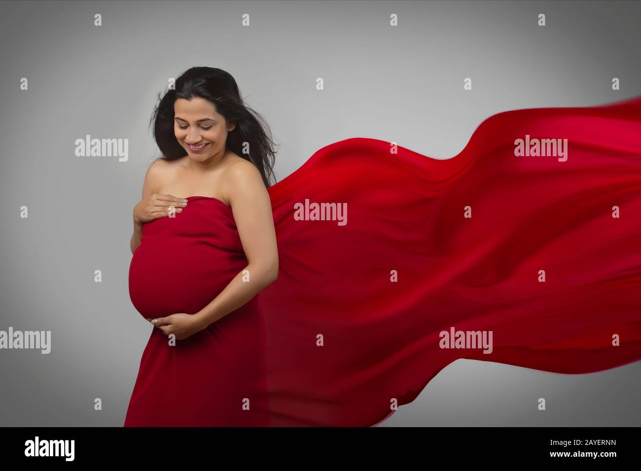 Pregnant woman with hands on her baby bump in a red dress. Stock Photo