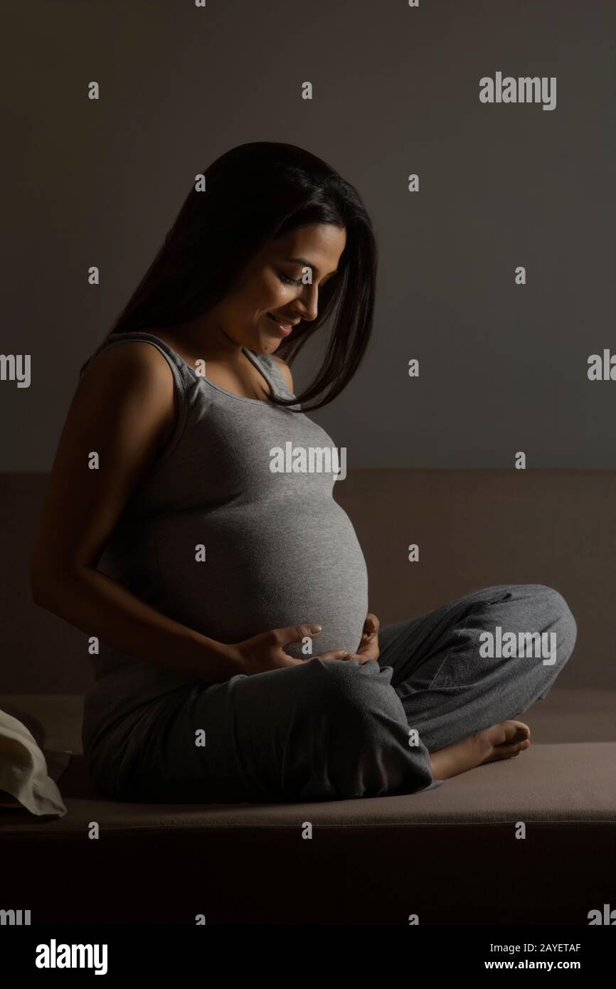 Pregnant woman sitting on the bed and holding her baby bump. Stock Photo