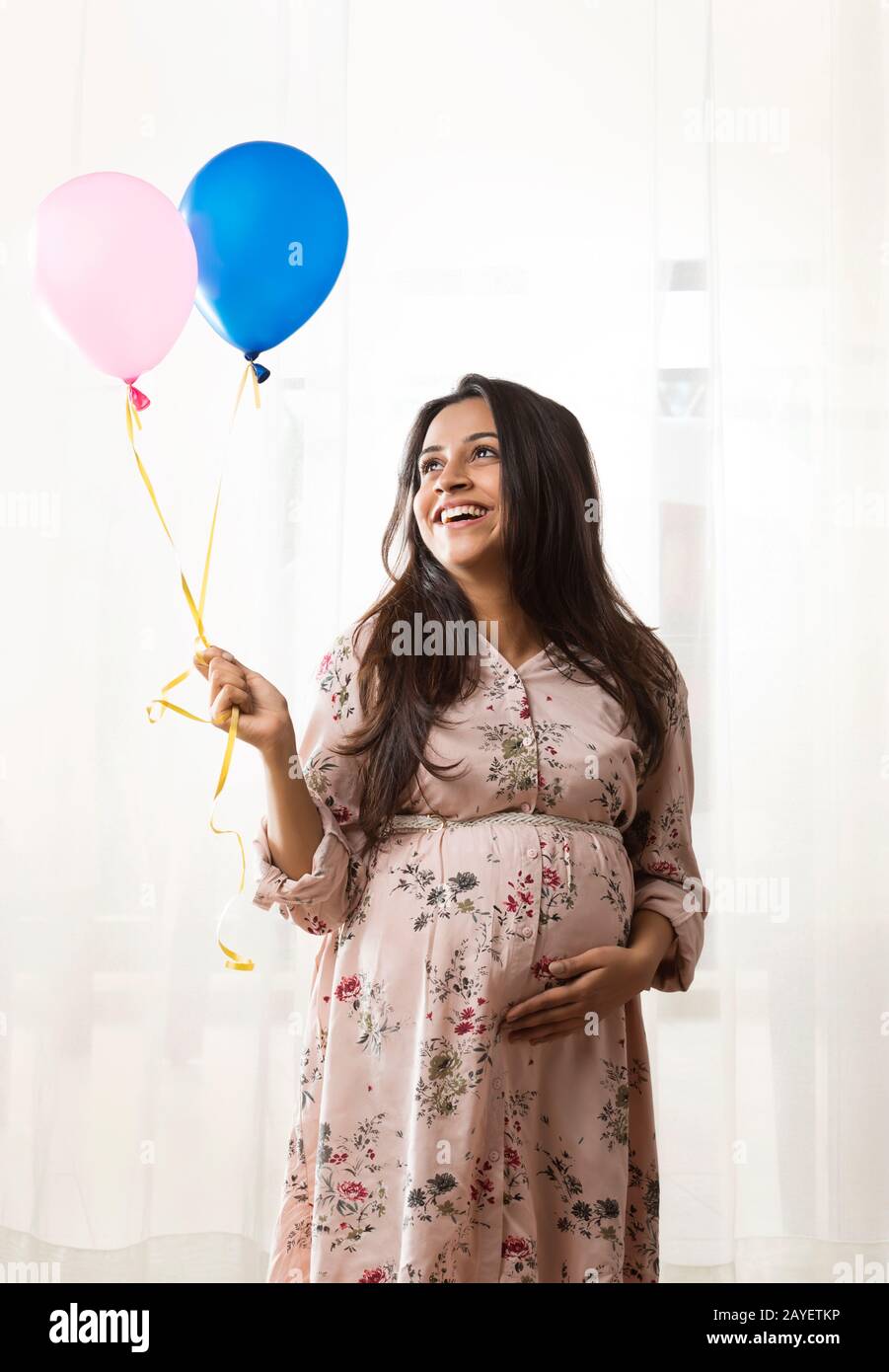 Pregnant woman smiling at the balloons in her hands. Stock Photo