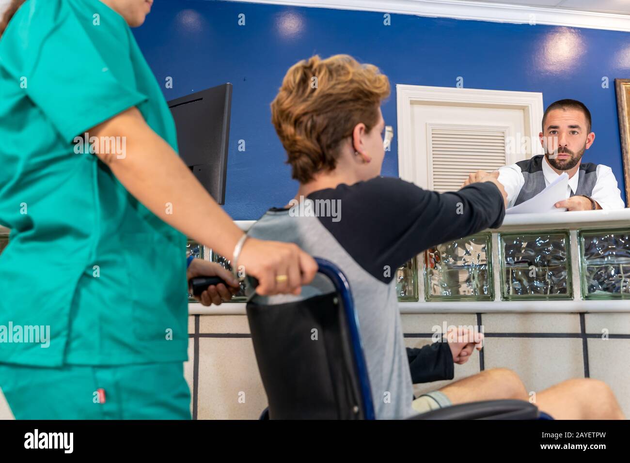 Stock photo of a boy in a wheelchair at a hospital reception attended by a receptionist Stock Photo