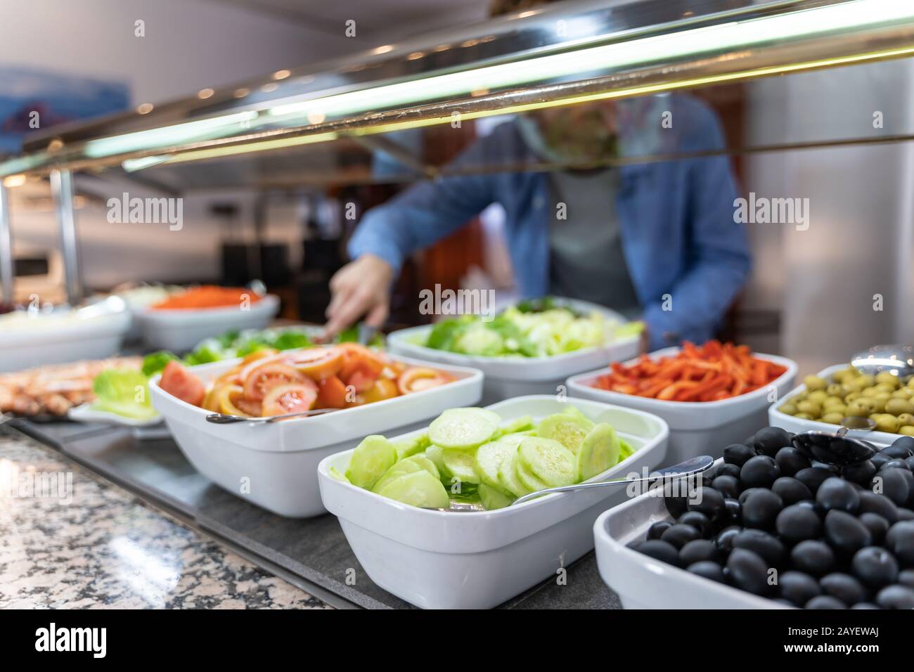 Stock photo of plates of healthy food, olives and salad and an unfocused background man picking up food. Lifestyle Stock Photo