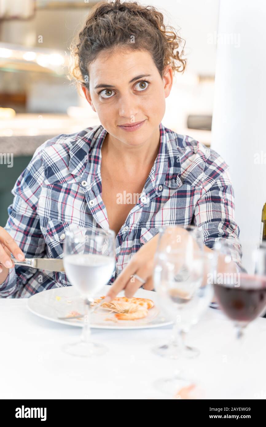 Stock vertical photo of a girl looking at her partner in front of her while eating shrimp in a restaurant. Lifestyle Stock Photo