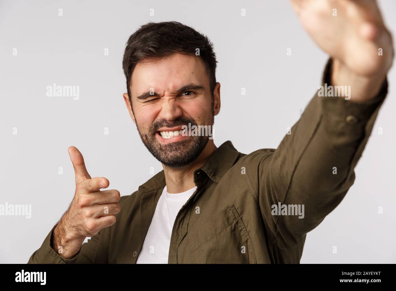 Cheeky and carefree confident handsome bearded guy, taking selfie as holding smartphone one hand, making pointing gesture as che Stock Photo