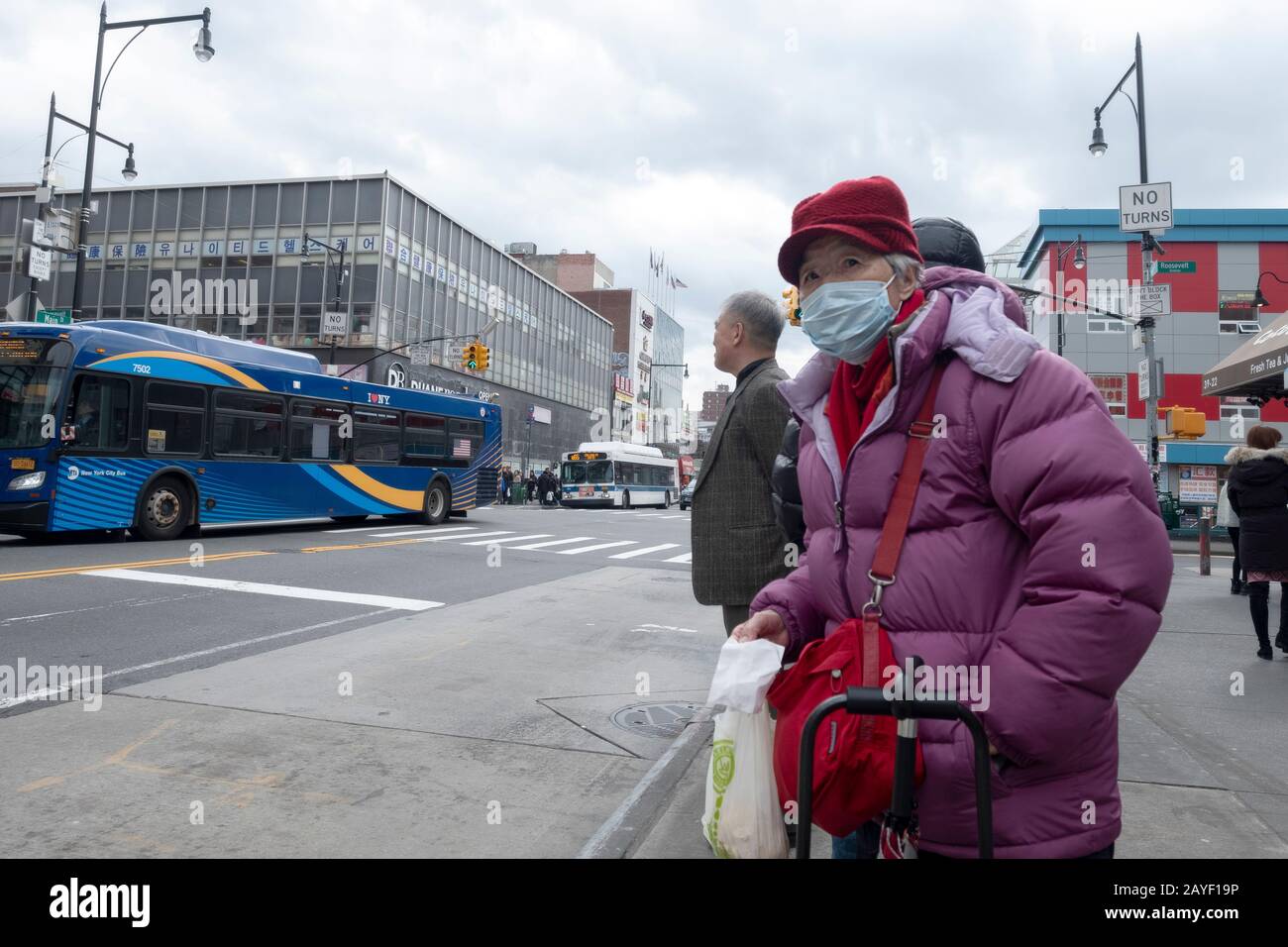 An older Chinese American woman out shopping waits for a bus on Main Street in Chinatown, Flushing, Queens, New York City. Stock Photo