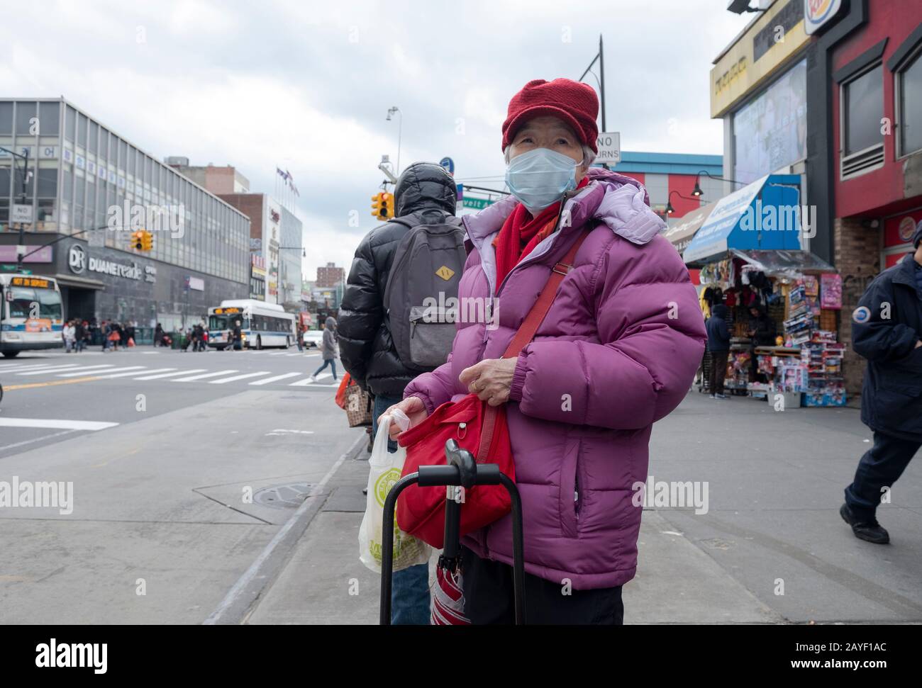 An older Chinese American woman out shopping waits for a bus on Main Street in Chinatown, Flushing, Queens, New York City. Stock Photo