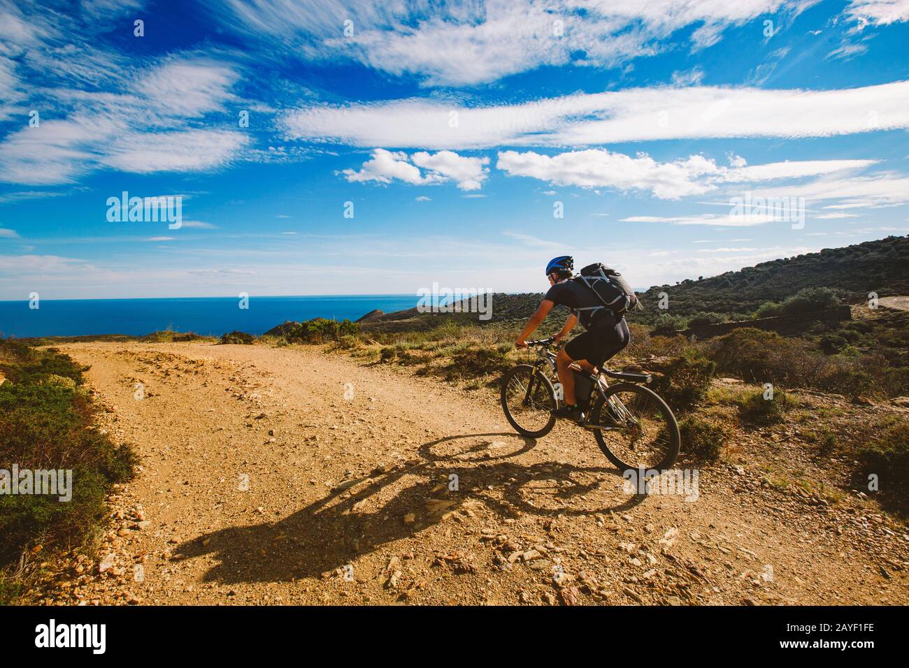 a young guy riding a mountain bike on a bicycle route in Spain on road against the background of the Mediterranean Sea. Dressed Stock Photo