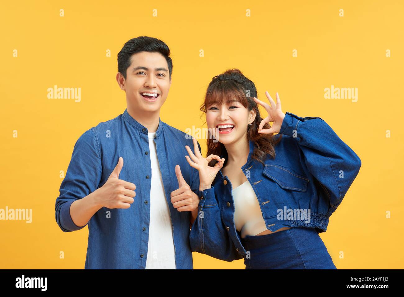 Excited beautiful asian couple shows thumb up gesture agree to do something and collaborate against orange wall, did great job, show approval, like id Stock Photo