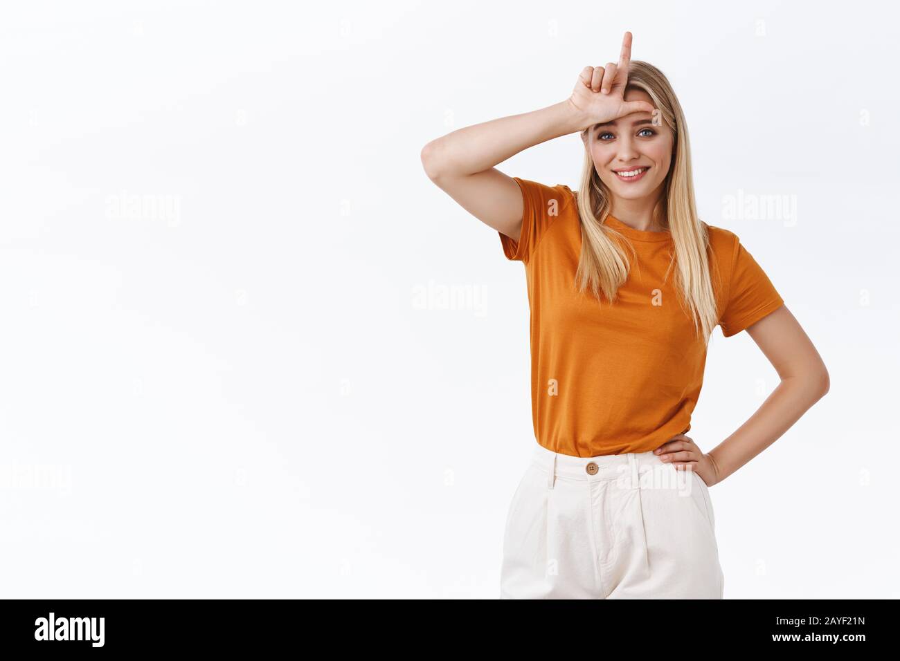Snobbish good-looking careless, stylish modern blond woman in orange t-shirt with tattoo, hold hand on waist, show loser L word on forehead and Stock Photo