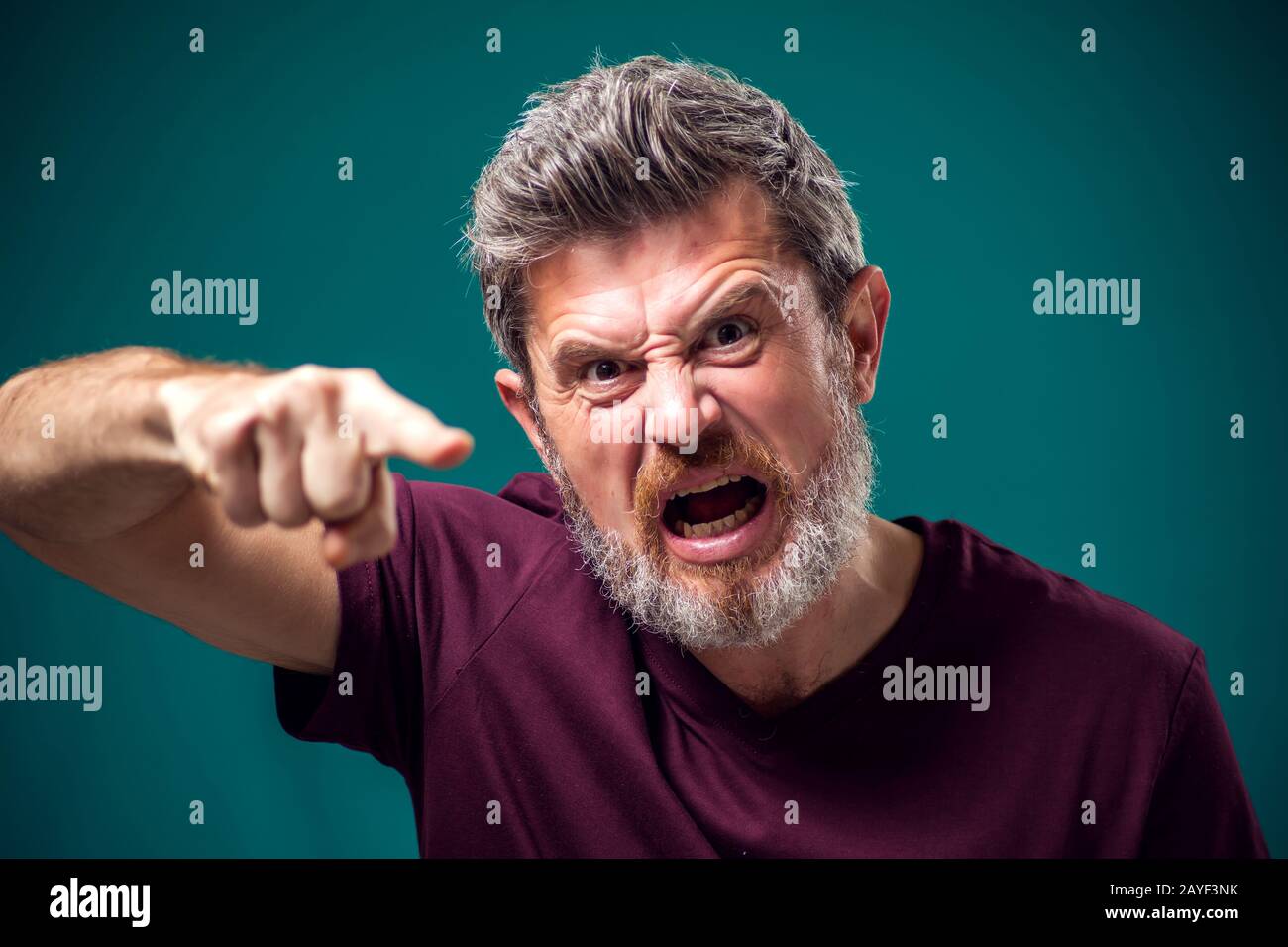 A portrait of angry bearded man in red t-shirt pointing finger at camera. People and emotions concept Stock Photo