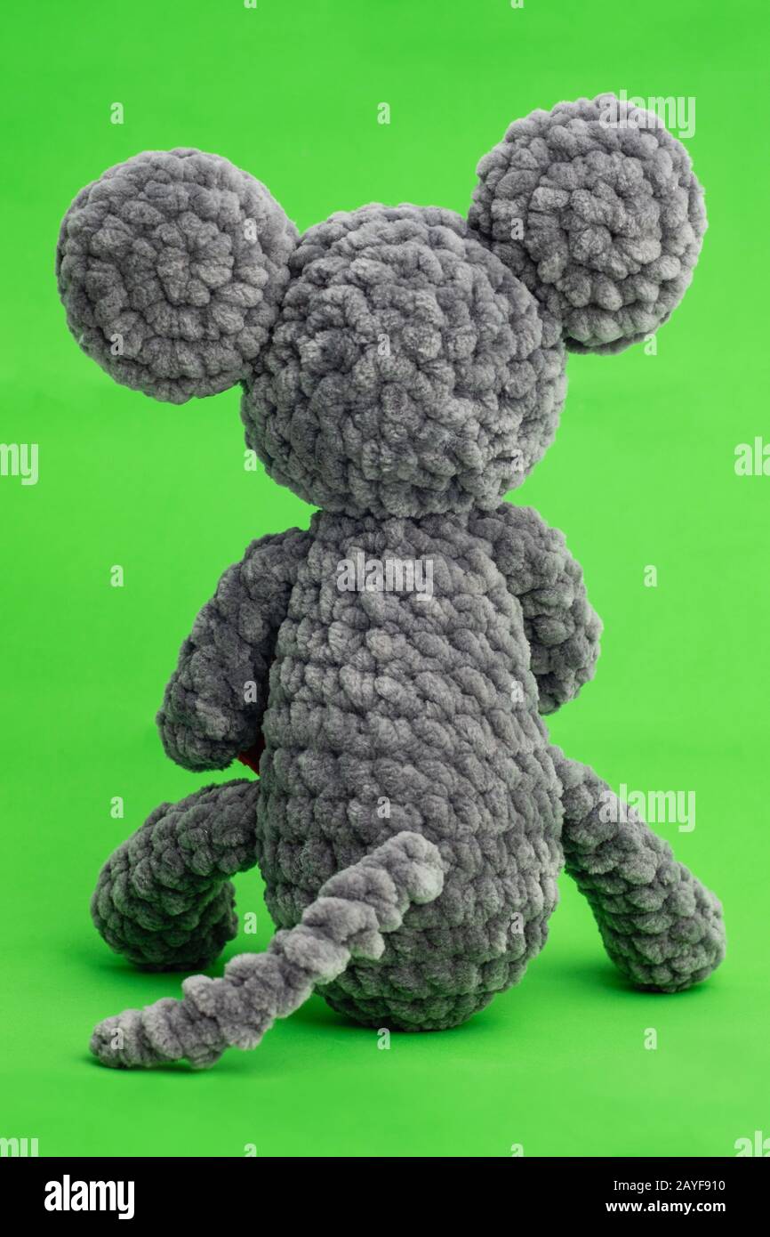 Grey knitted mouse with a heart in hand on a green background, rear view Stock Photo