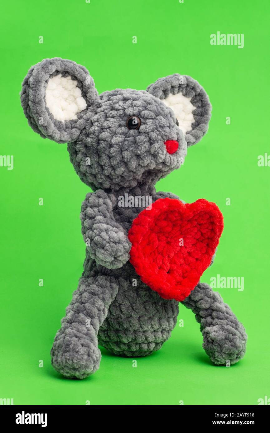 Grey knitted mouse with a heart in hand on a green background, side view Stock Photo