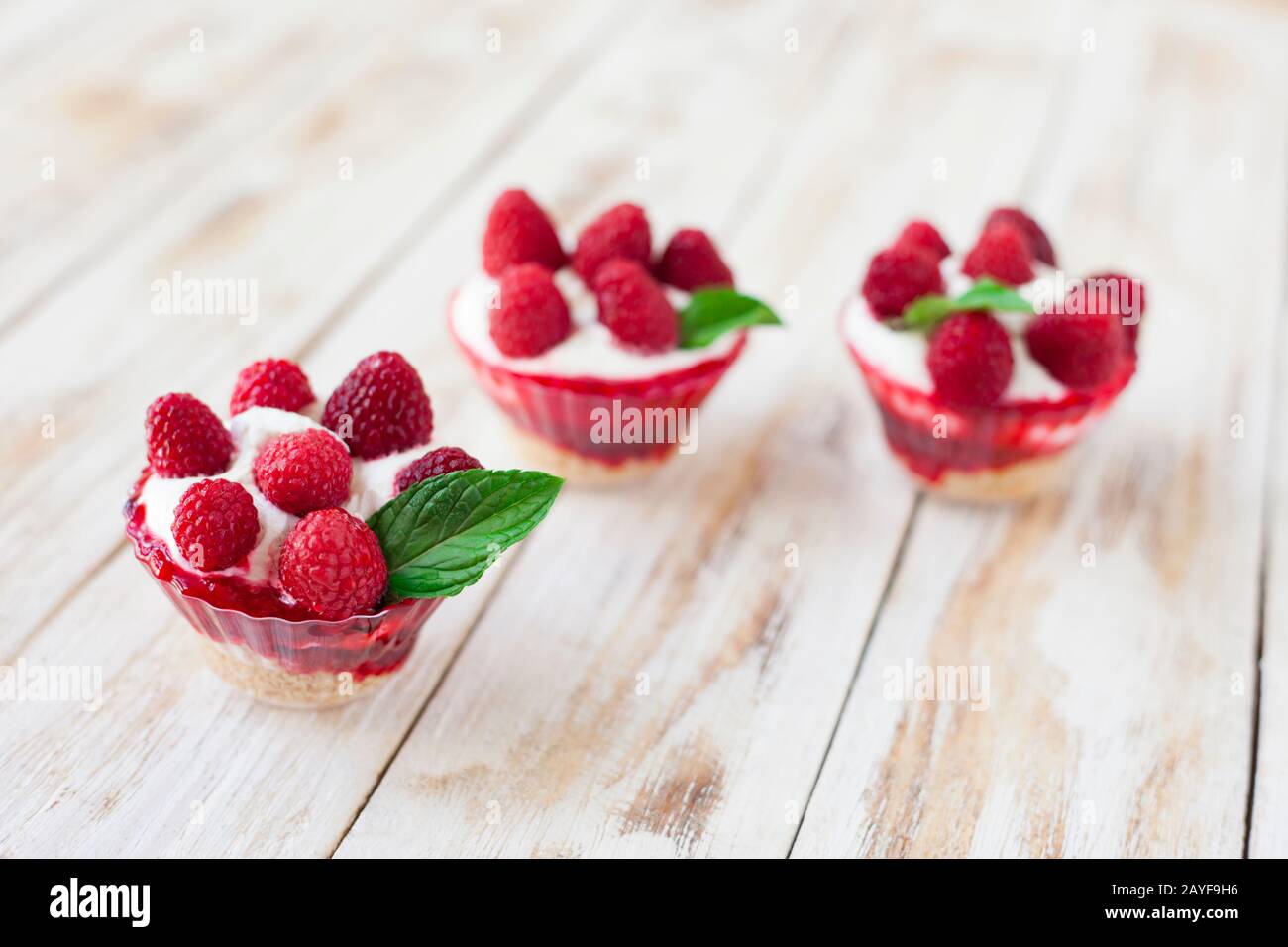 Trifle with raspberries, mint and cheesecake on old wooden white background. English traditional sweet dessert. Stock Photo