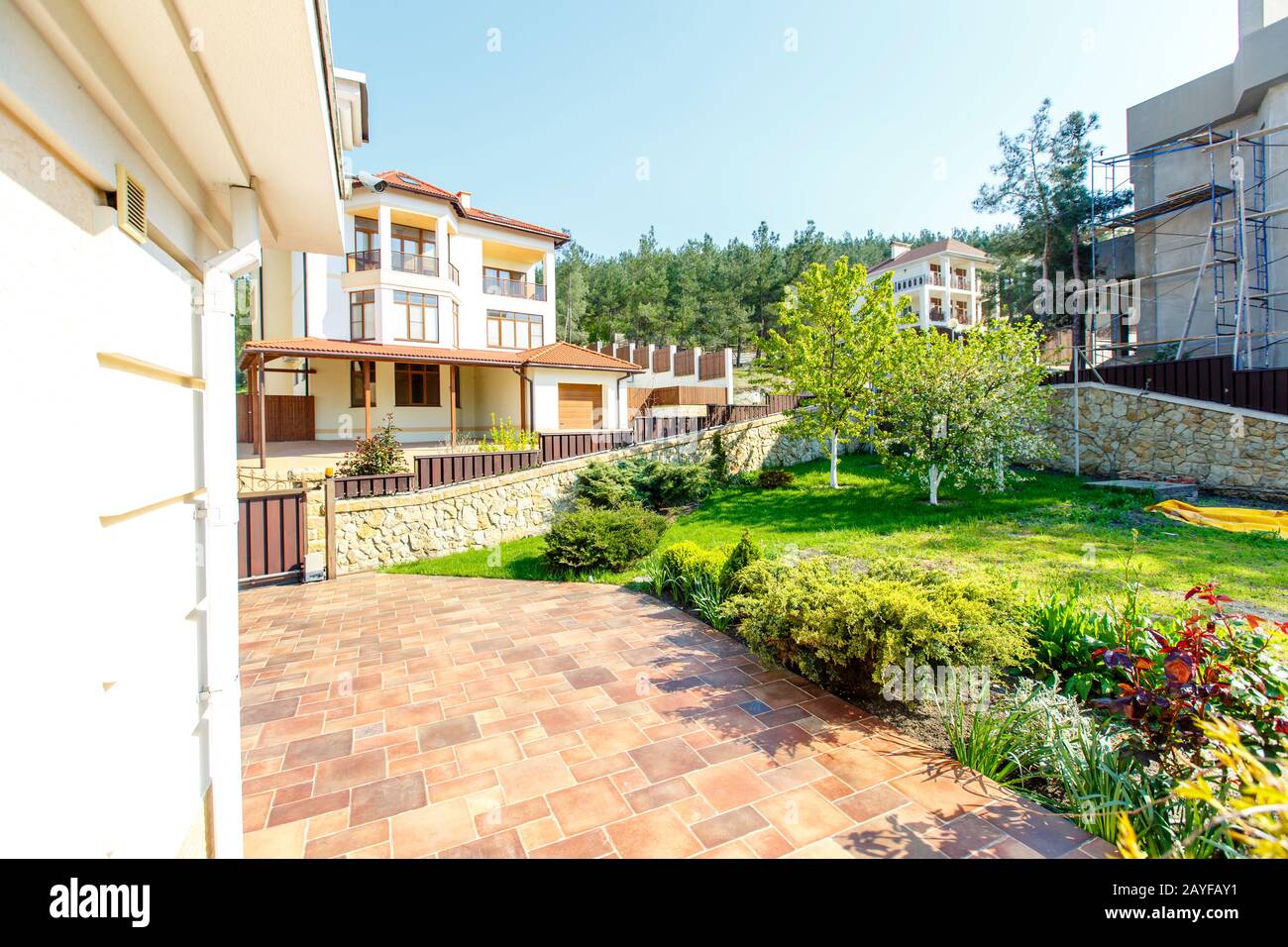 Lawn with green cut grass in the back yard of the cottage. The white walls of the cottage, columns, trees. Juicy spring greens. Laksheri. Stock Photo