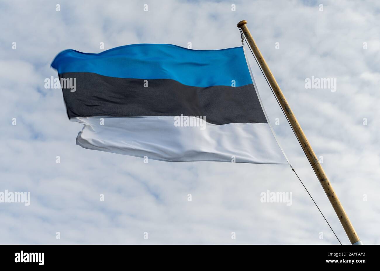 The developing white-black-blue flag of Estonia against the background of clouds in the sky. Stock Photo