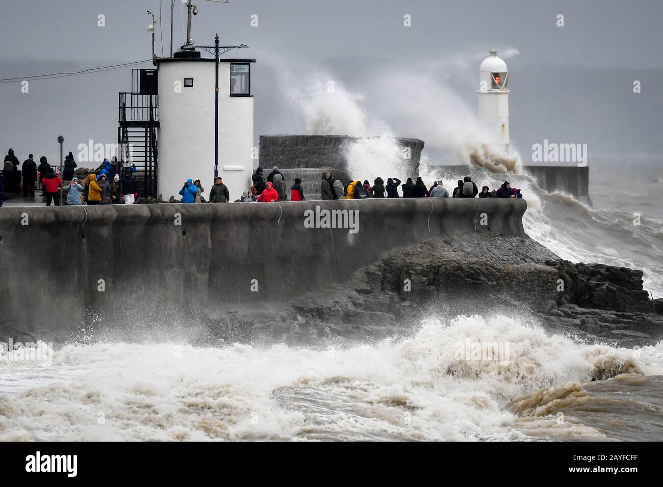 People watch waves and rough seas pound against the harbour wall at Porthcawl, Wales, as the UK is braced for widespread weather disruption for the second weekend in a row as Storm Dennis sweeps in. Stock Photo