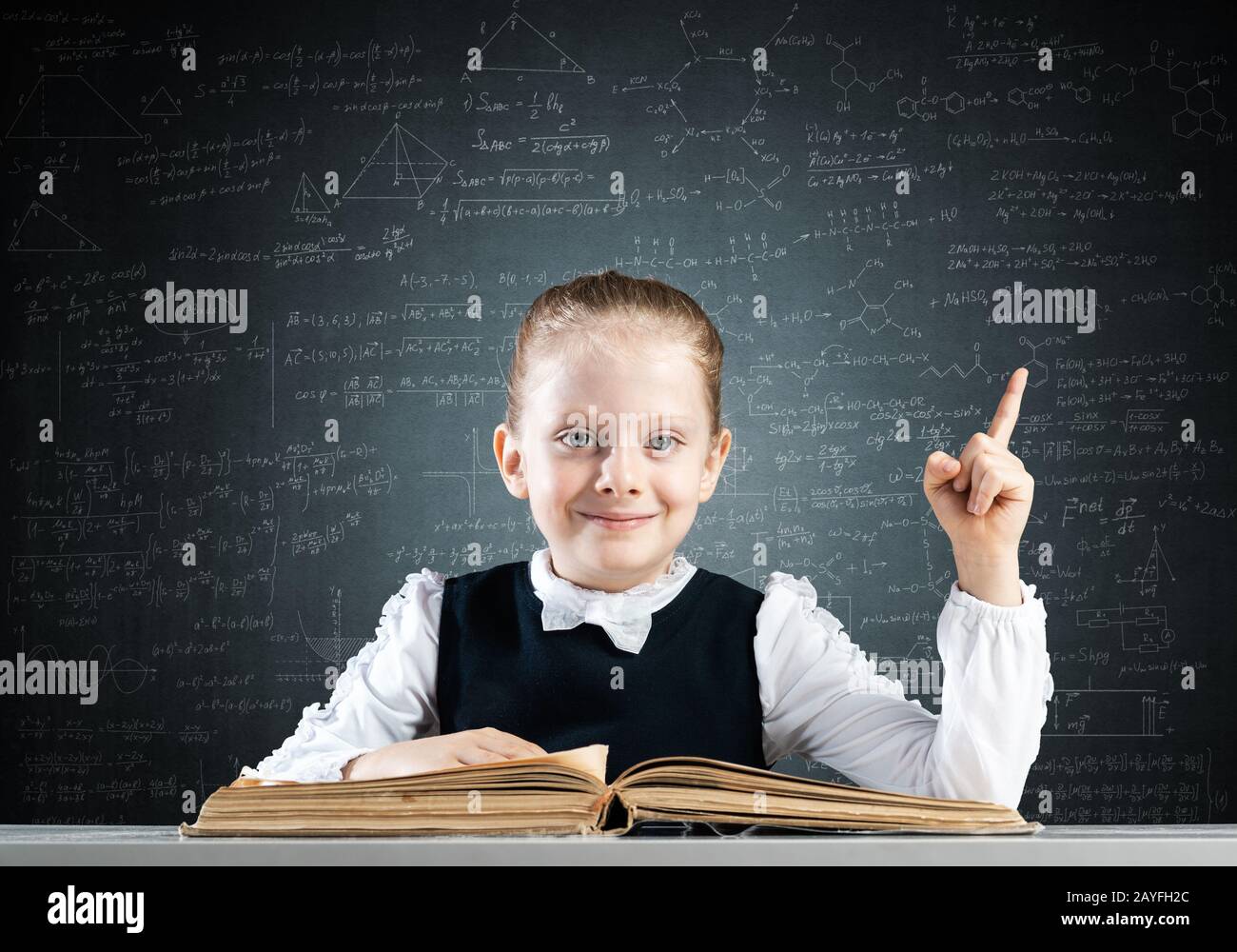 Smiling little girl sitting at desk with open book Stock Photo - Alamy