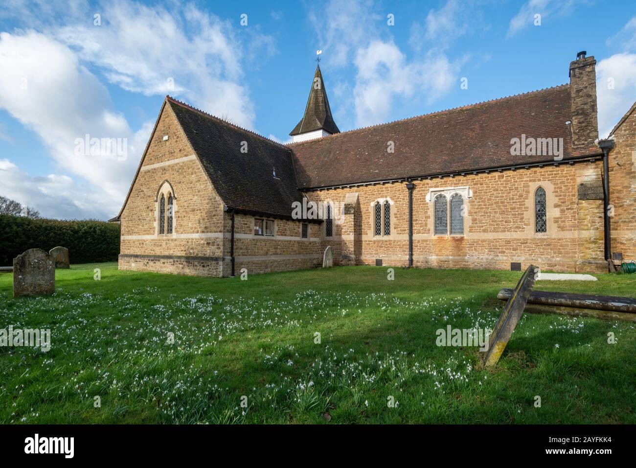 St James parish church in Elstead village, Surrey, UK, with snowdrops during February Stock Photo