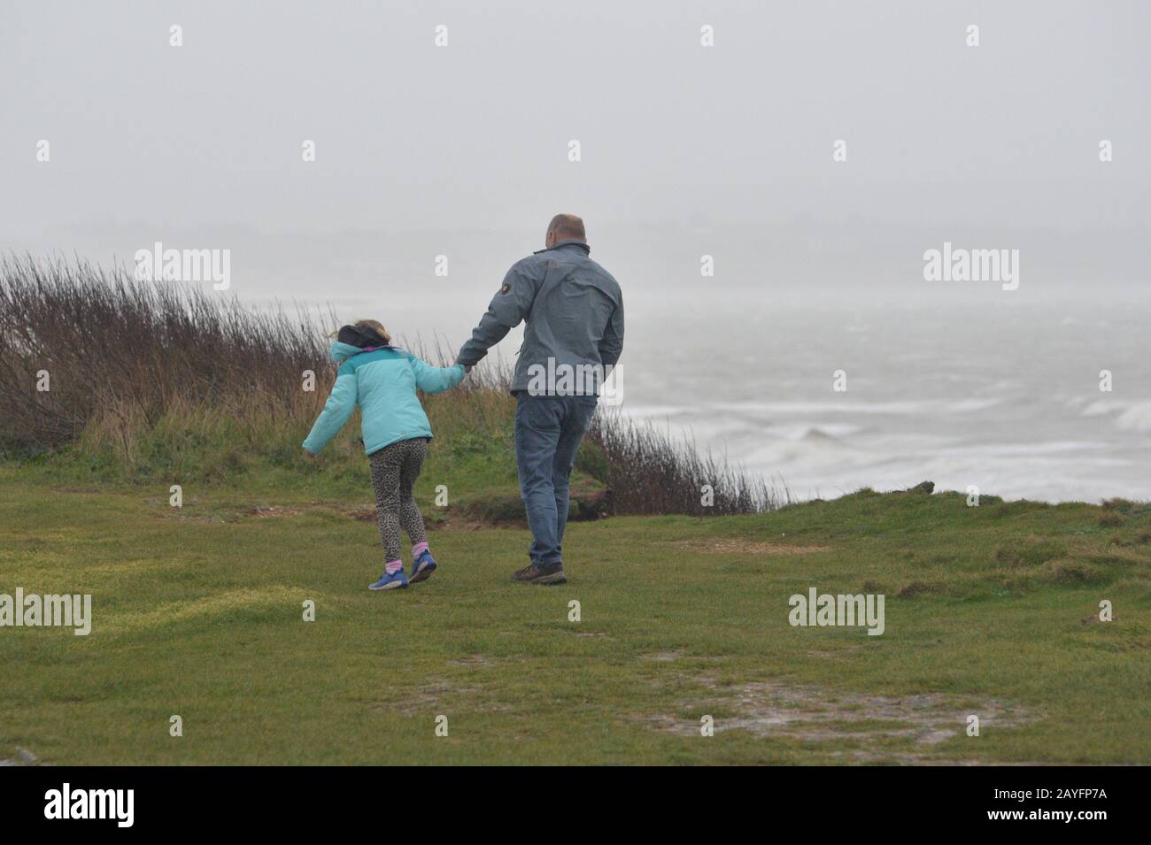 Storm Dennis, classified as a bomb cyclone, brings gale force winds and heavy rain to the south coast. The strong wind whips up the sea into huge waves. People leaning into the wind on the clifftop, Milford-on-Sea, Hampshire, England, UK, 15th February 2020, Weather: Stock Photo