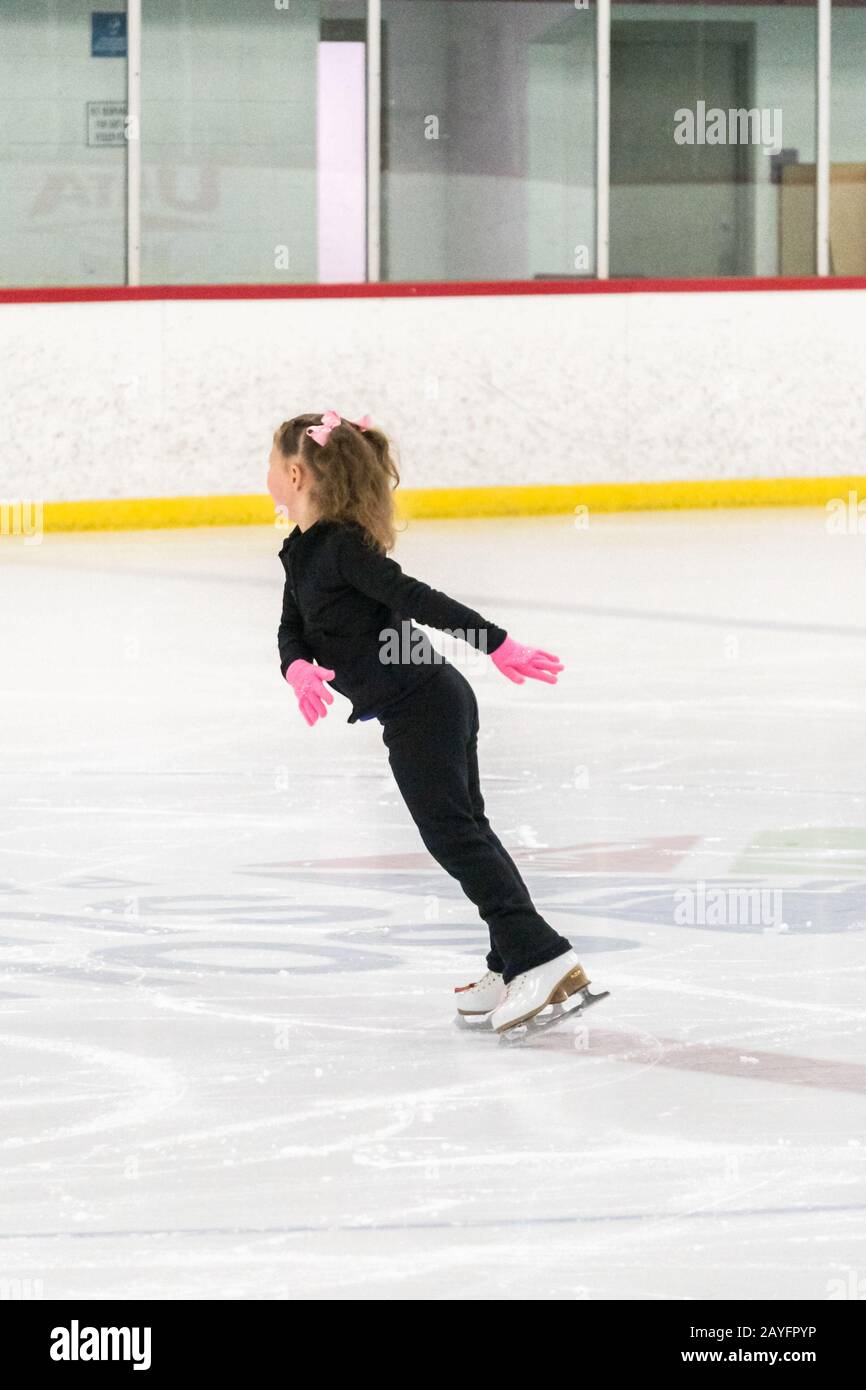 Little girl practicing figure skating moves on the indoor ice rink