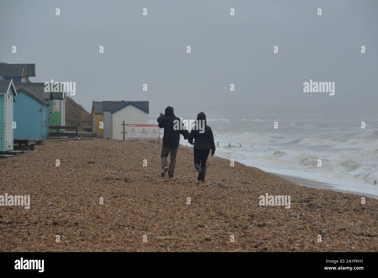 Storm Dennis, classified as a bomb cyclone, brings gale force winds and heavy rain to the south coast. The strong wind whips up the sea into huge waves. Couple walking on the beach in the windy weather, Milford-on-Sea, Hampshire, England, UK, 15th February 2020. Stock Photo