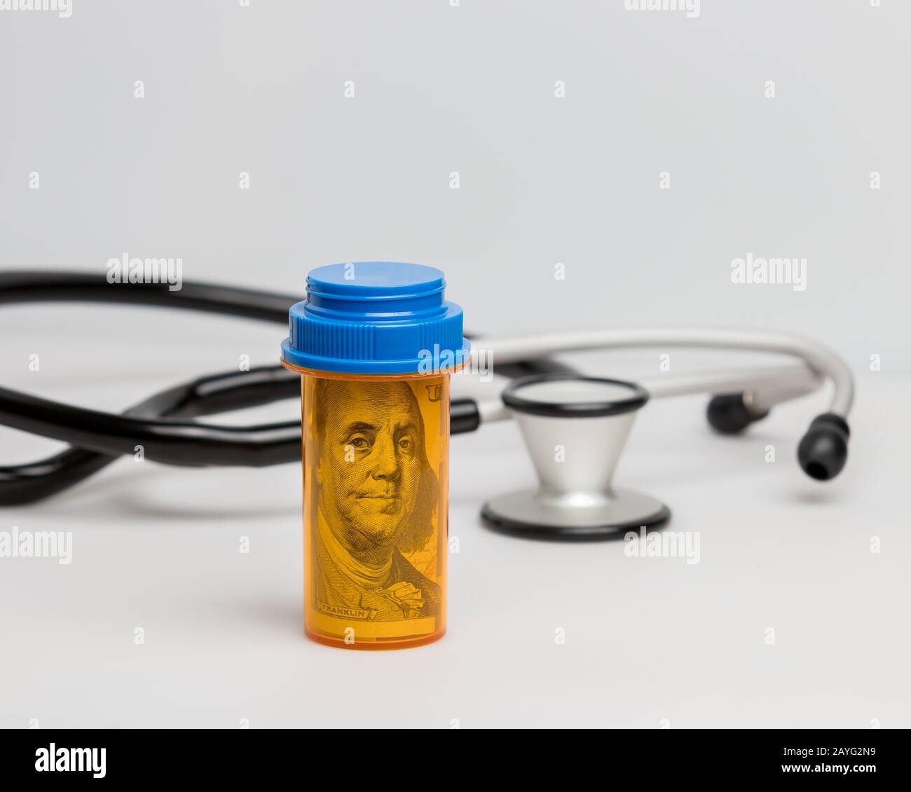 Prescription drug medicine pill bottle with 100 dollar bill and stethoscope on white background. Concept of drug, health care, and medical insurance Stock Photo