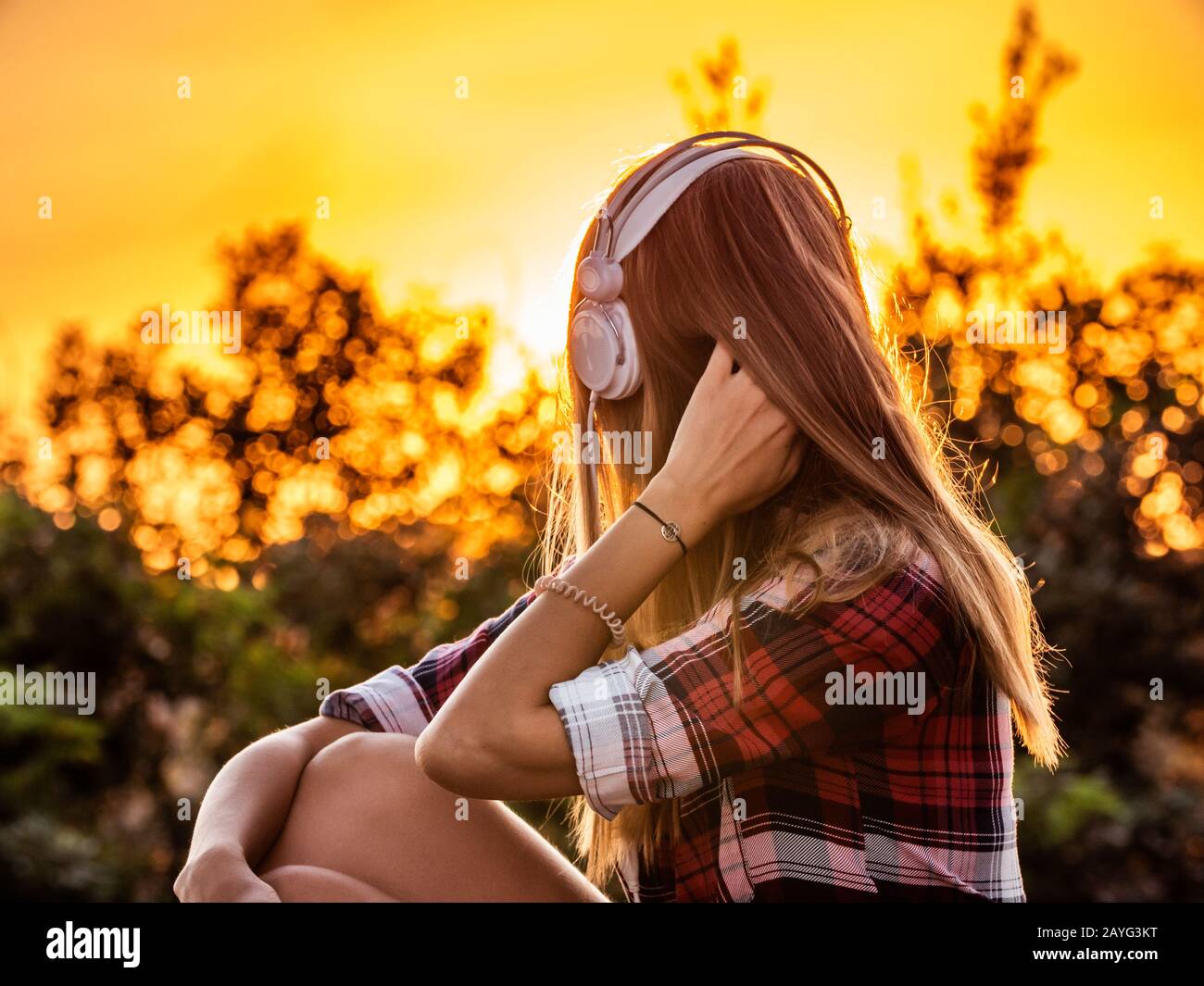 Happy young blonde woman with long hair and blue eyes listening to music with white headpones sitting outside at sunset Stock Photo - Alamy Happy young blonde woman with long hair and blue eyes listening to music with white headpones sitting outside at sunset Stock Photo - Alamy