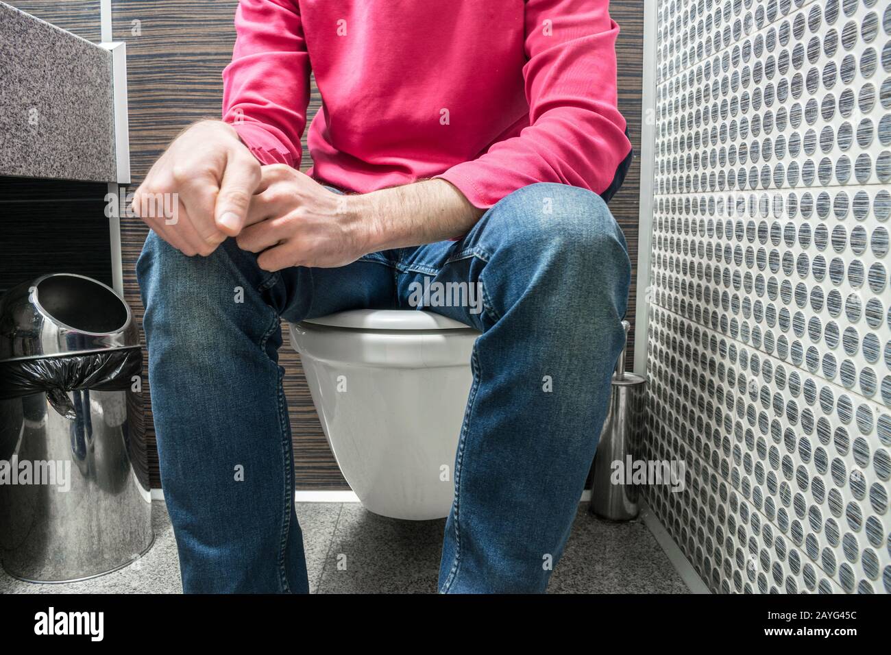 A man in jeans is sitting on the toilet in a public toilet Stock Photo