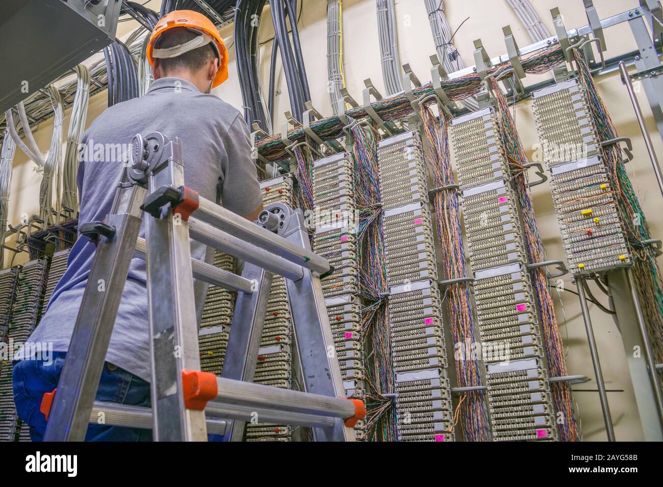 The man is laying the cable in the server room of the data center. The engineer standing on the stairs works with the switching equipment of the telep Stock Photo