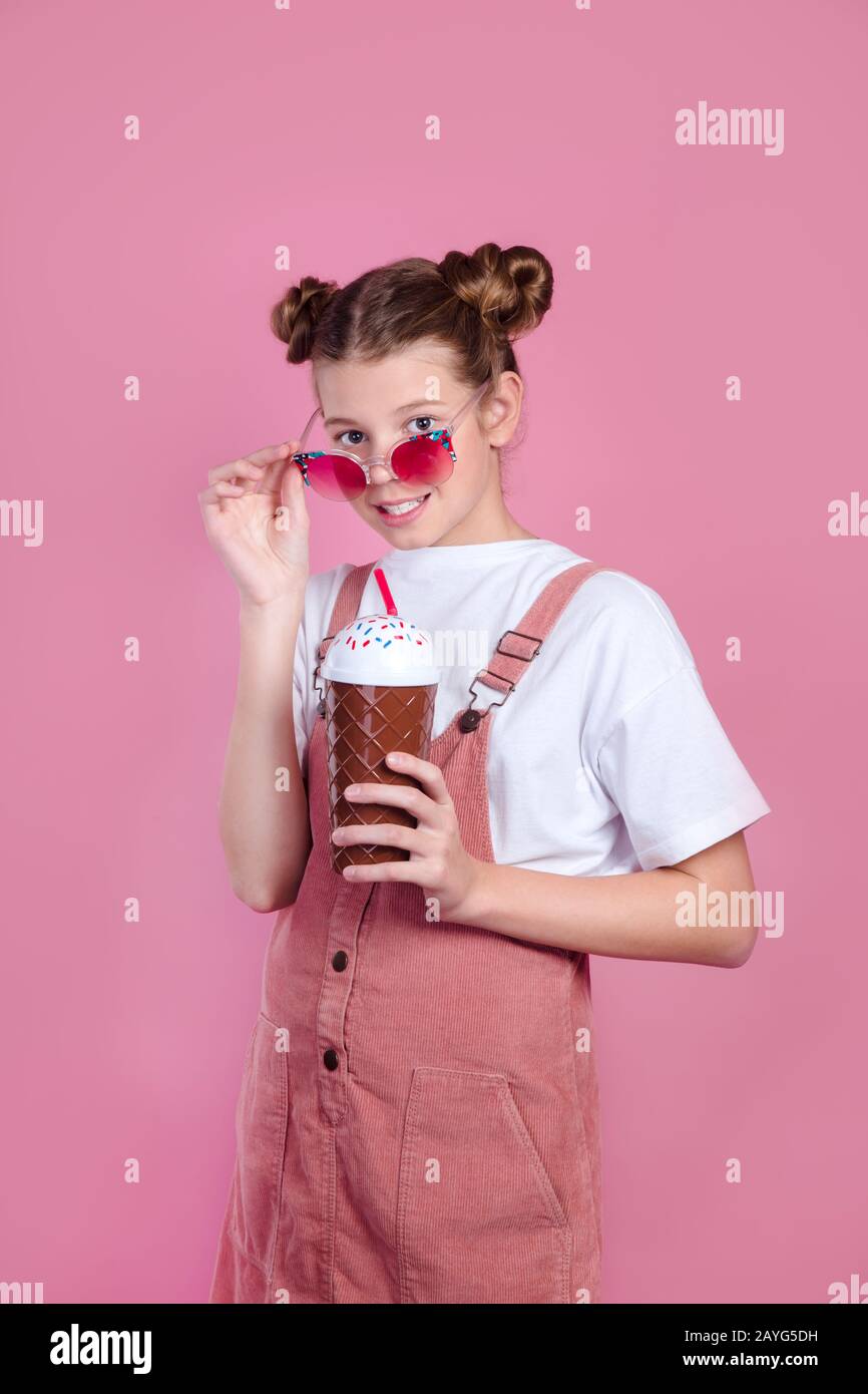 kid girl looking camera lowering sunglasses and drinking cocktail. Summer concept Stock Photo