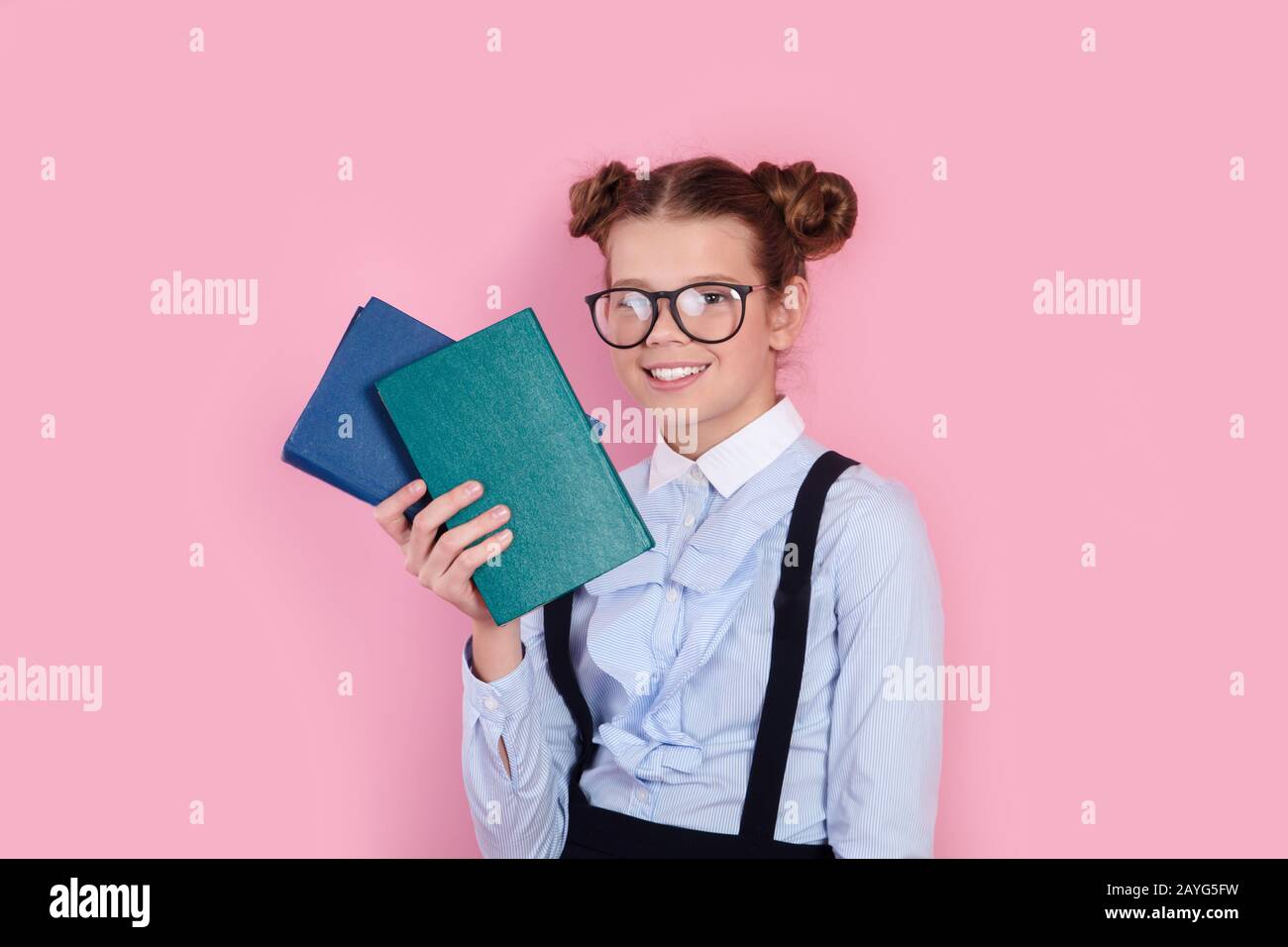 Young girl in school uniform and glasses holding books in her hands on pink background Stock Photo