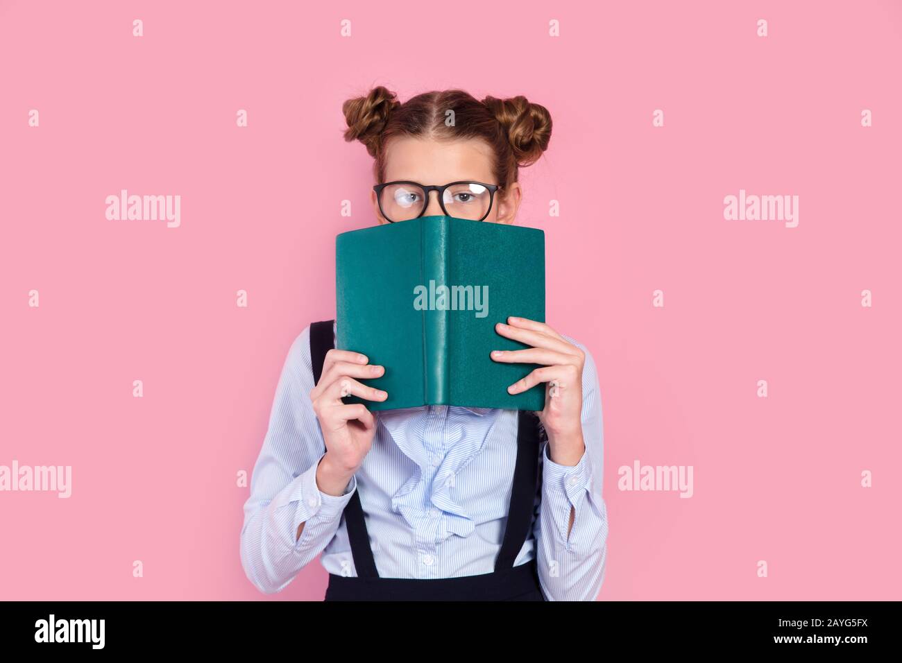 Young girl in school uniform and glasses holding book in front of her face Stock Photo