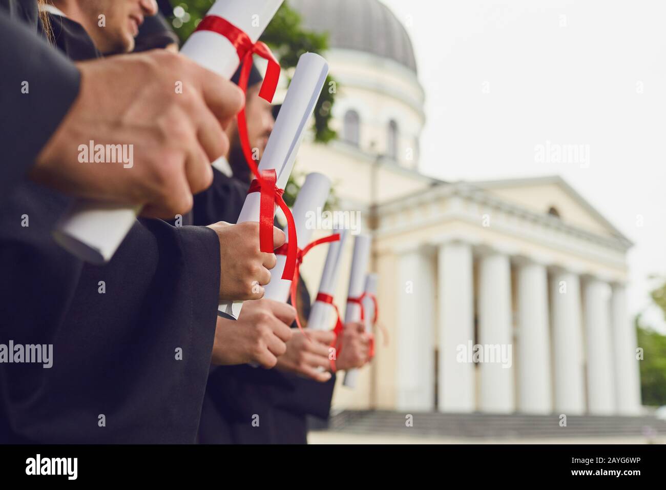 Scrolls of diplomas in the hands of a group of graduates. Stock Photo