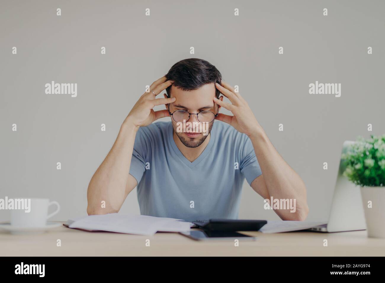 Young European male dressed casually, has debt problems, not able to pay out all debts, studies papers from bank, has frustrated look, tries to manage Stock Photo