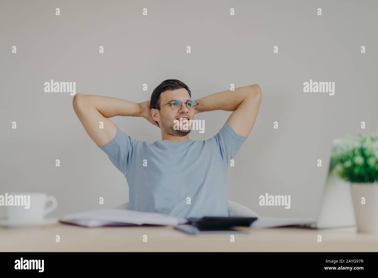 Carefree male enterpreneur ready with financial report, being glad to realize that he recieves high net profit, sits at working desk with calculator, Stock Photo