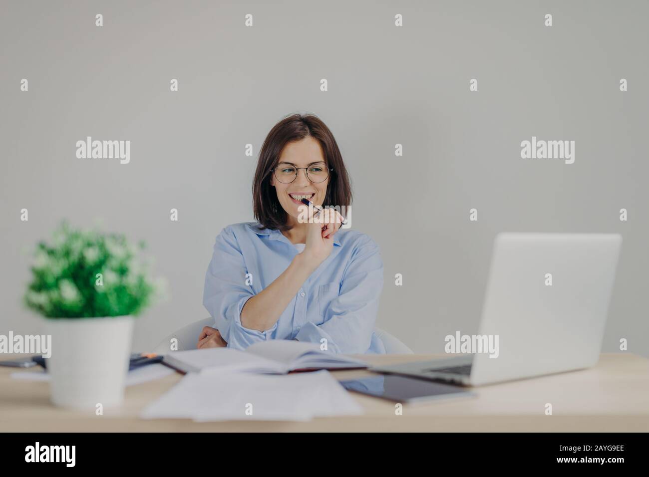 Intelligent gorgeous female dressed casually works at home, sits in front of opened laptop, has happy expression as sees solution of problems, keeps p Stock Photo