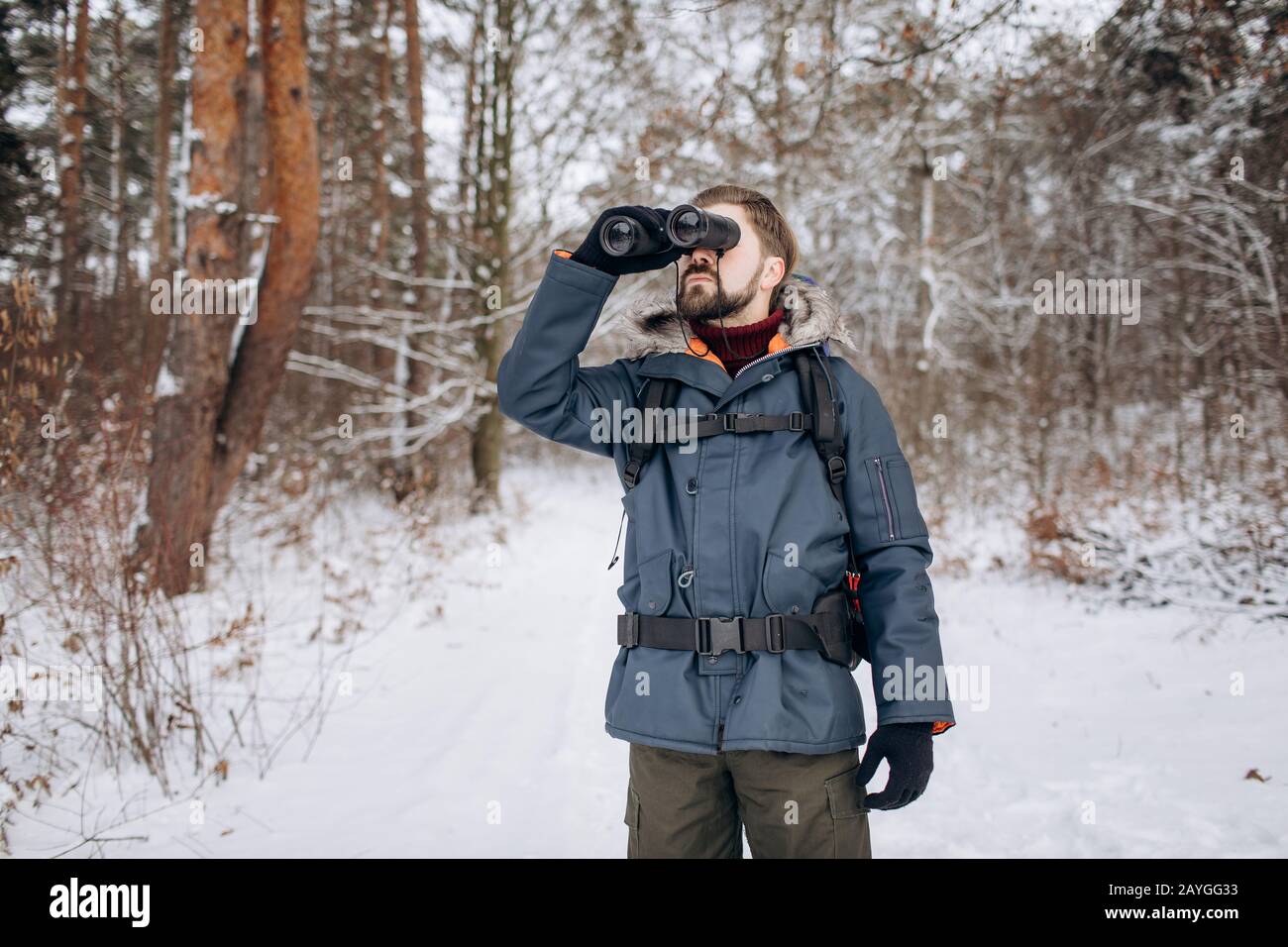 Tourist ranger in fur hood anorak looking into the distance using binoculars Stock Photo