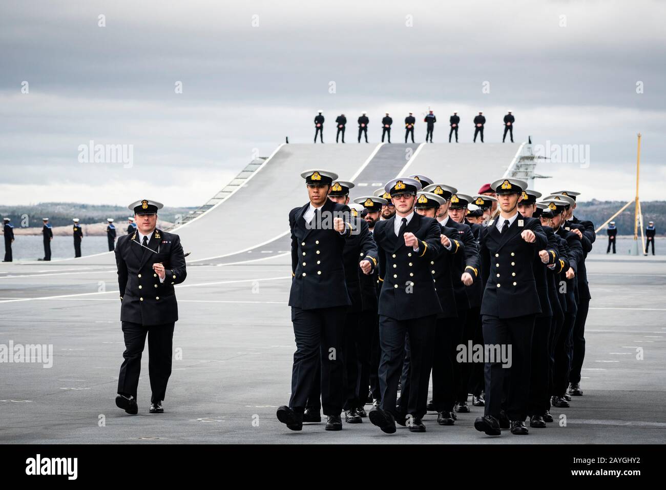Sailors marching as others man the rails of the Royal Navy's aircraft