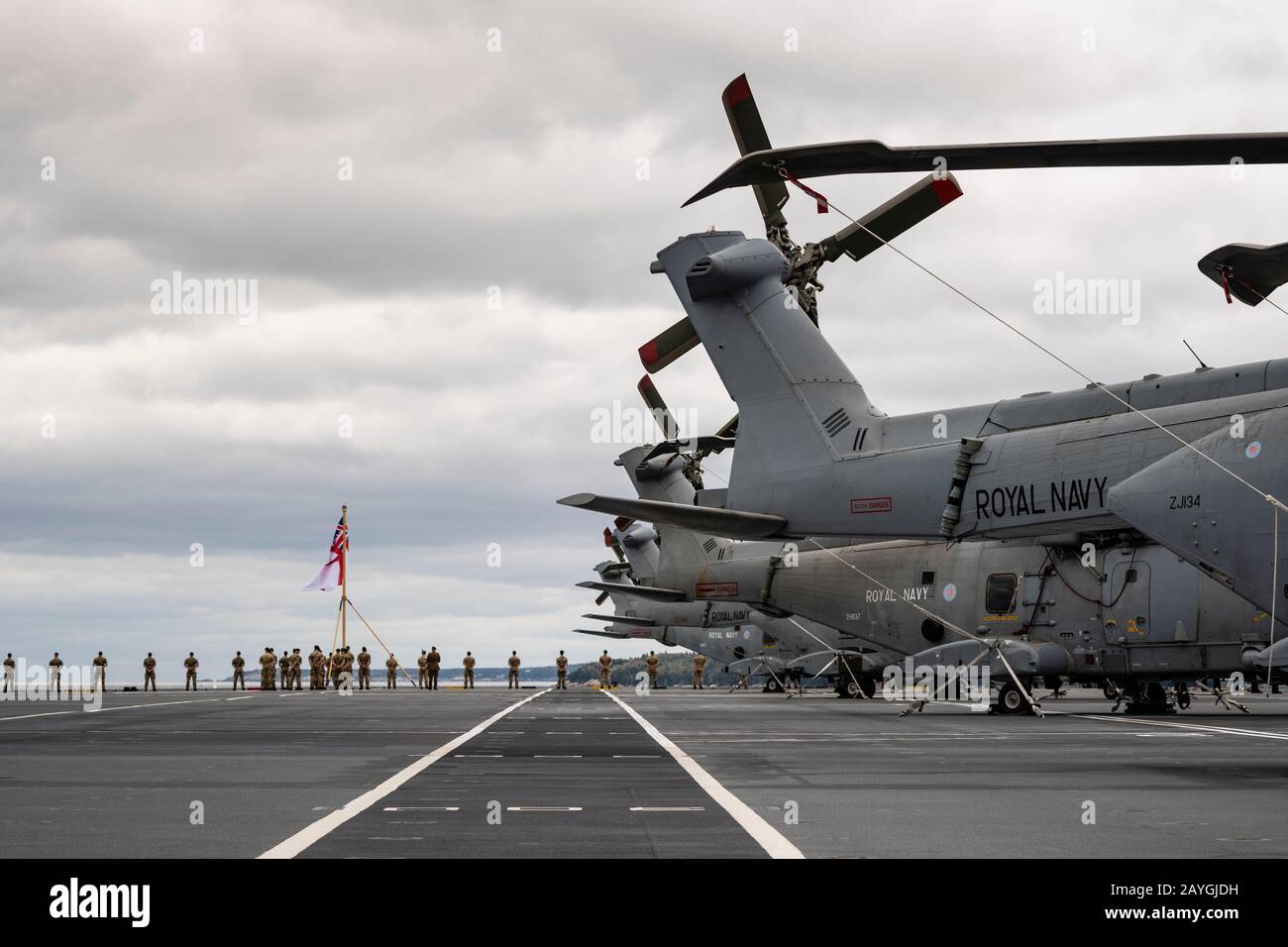 The tails of lined up Royal Navy Merlin helicopters aboard the carrier HMS QUEEN ELIZABETH with Royal Marines lining the rail in the background. Stock Photo