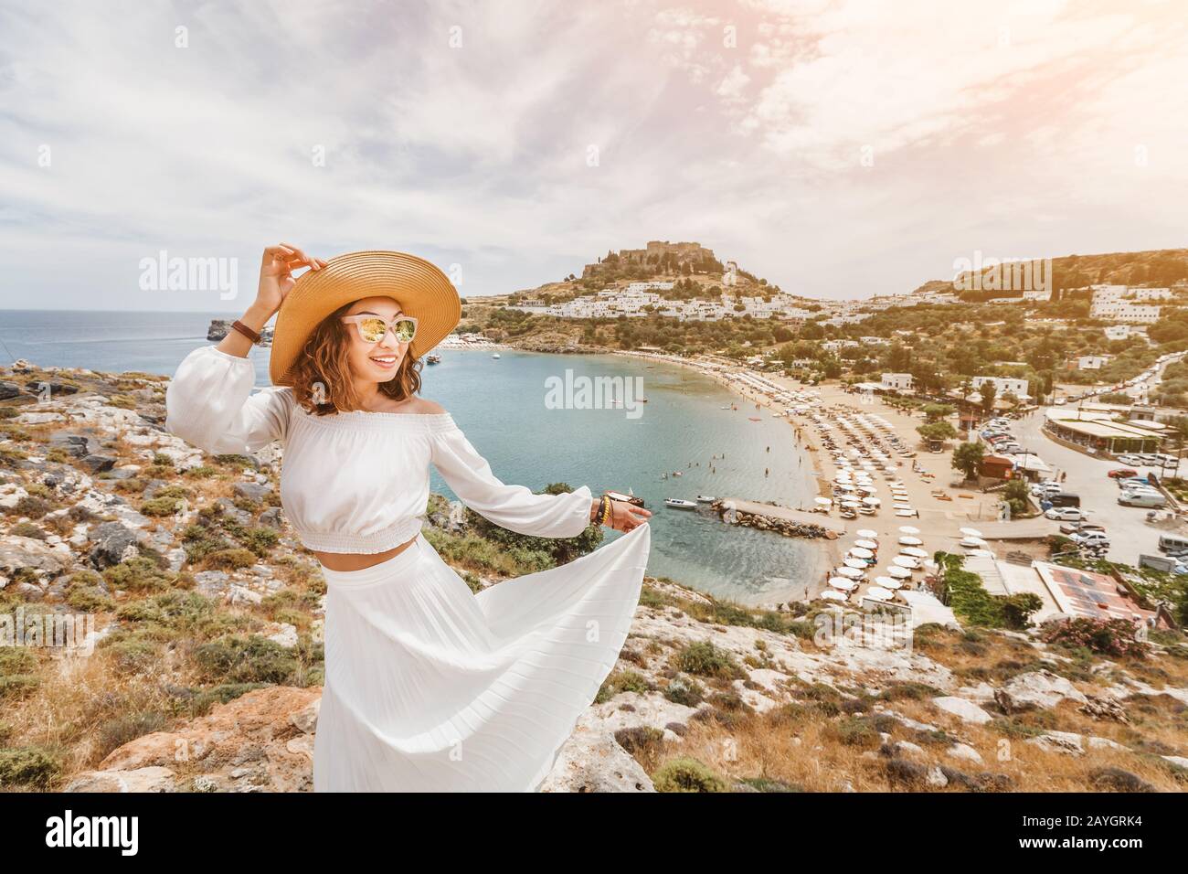 Happy asian woman travels in Greece. Having fun at the stunning view on sea resort and old town of Lindos on the mountain Stock Photo