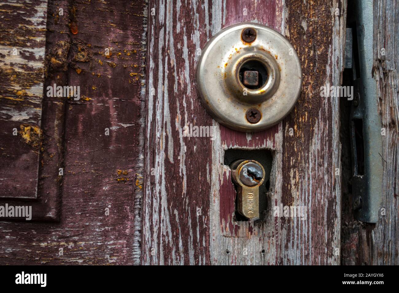 Part of a brown old door with a broken handle and a door lock. The paint on the door faded and crumbled. Closeup photo of front Stock Photo