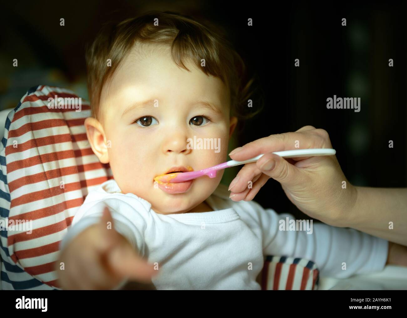The one-year-old child eats porridge and points his finger at the camera Stock Photo