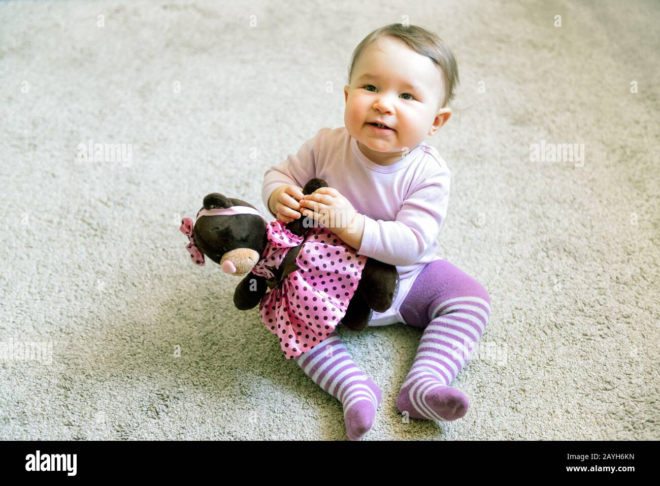 Happy baby girl plays with toy bear on the floor at home Stock Photo