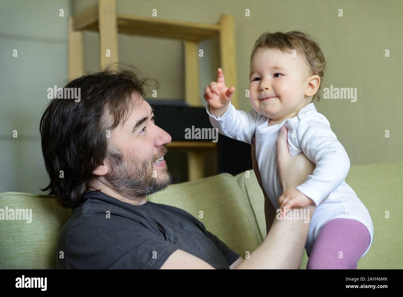 Happy baby plays with father on the couch at home. Baby points his finger. Stock Photo