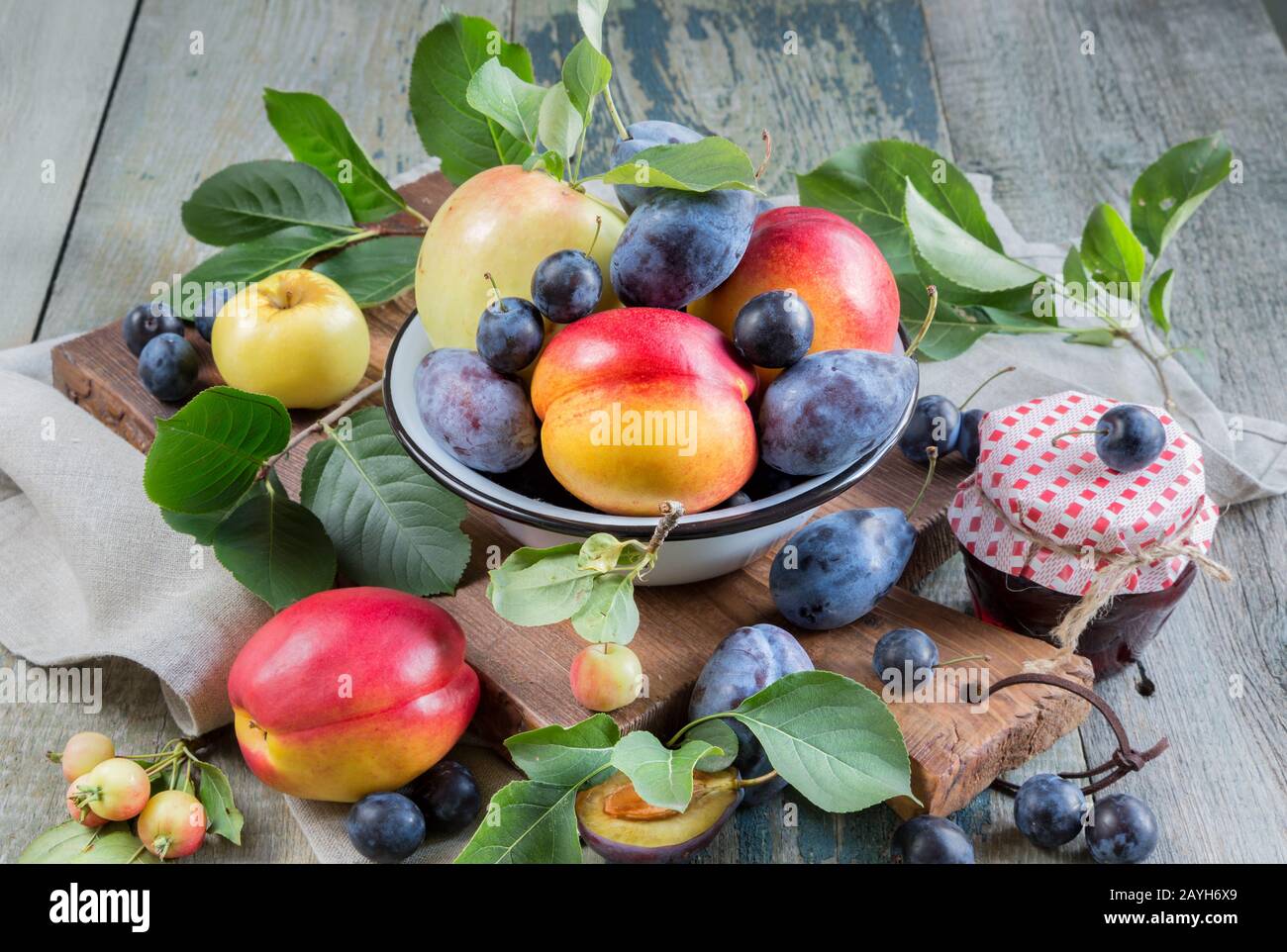 Several red nectarines with green leaves, blue plums and prunes in a enamelled bowl on the old wooden table Stock Photo