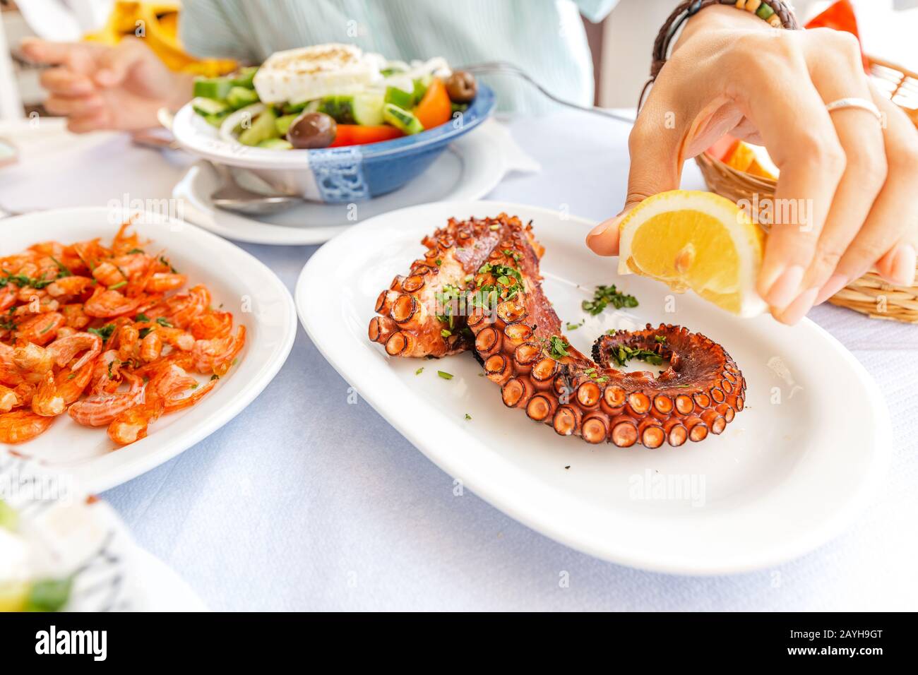 Close-up of a woman eating delicious seafood - shrimp and octopus grilled and vegetable salad. The concept of Mediterranean cuisine and healthy food Stock Photo