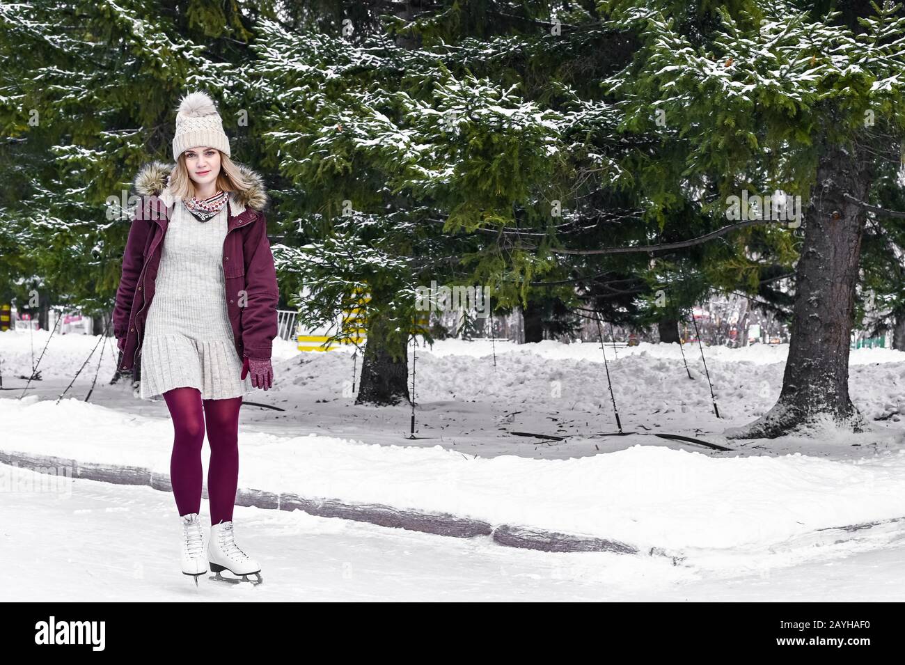 Young blonde caucasian girl in warm clothes skating on frozen lake in snowy winter park. Winter holidays concept Stock Photo
