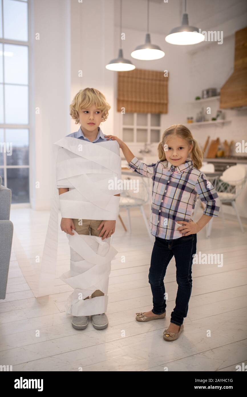 Two kids playing toilet paper mummy game at home Stock Photo