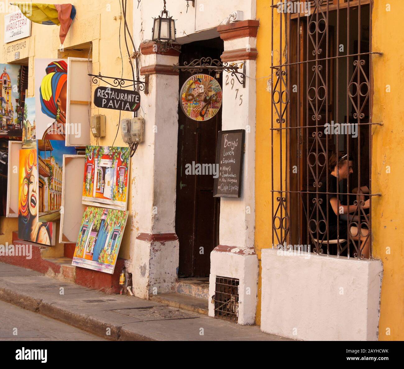 Colorful paintings displayed for sale outside an art gallery and the Pavia Restaurant in Getsemani, Cartagena, Colombia Stock Photo