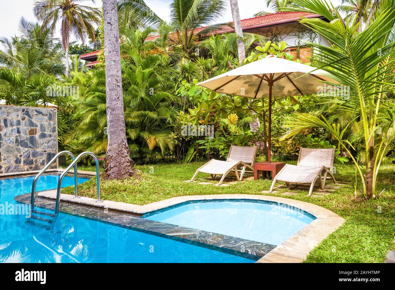 Sri Lanka - October 31, 2017: Pool with umbrella and beach beds in a tropical hotel or house. Beautiful swimming pool in backyard. Pool with blue clea Stock Photo